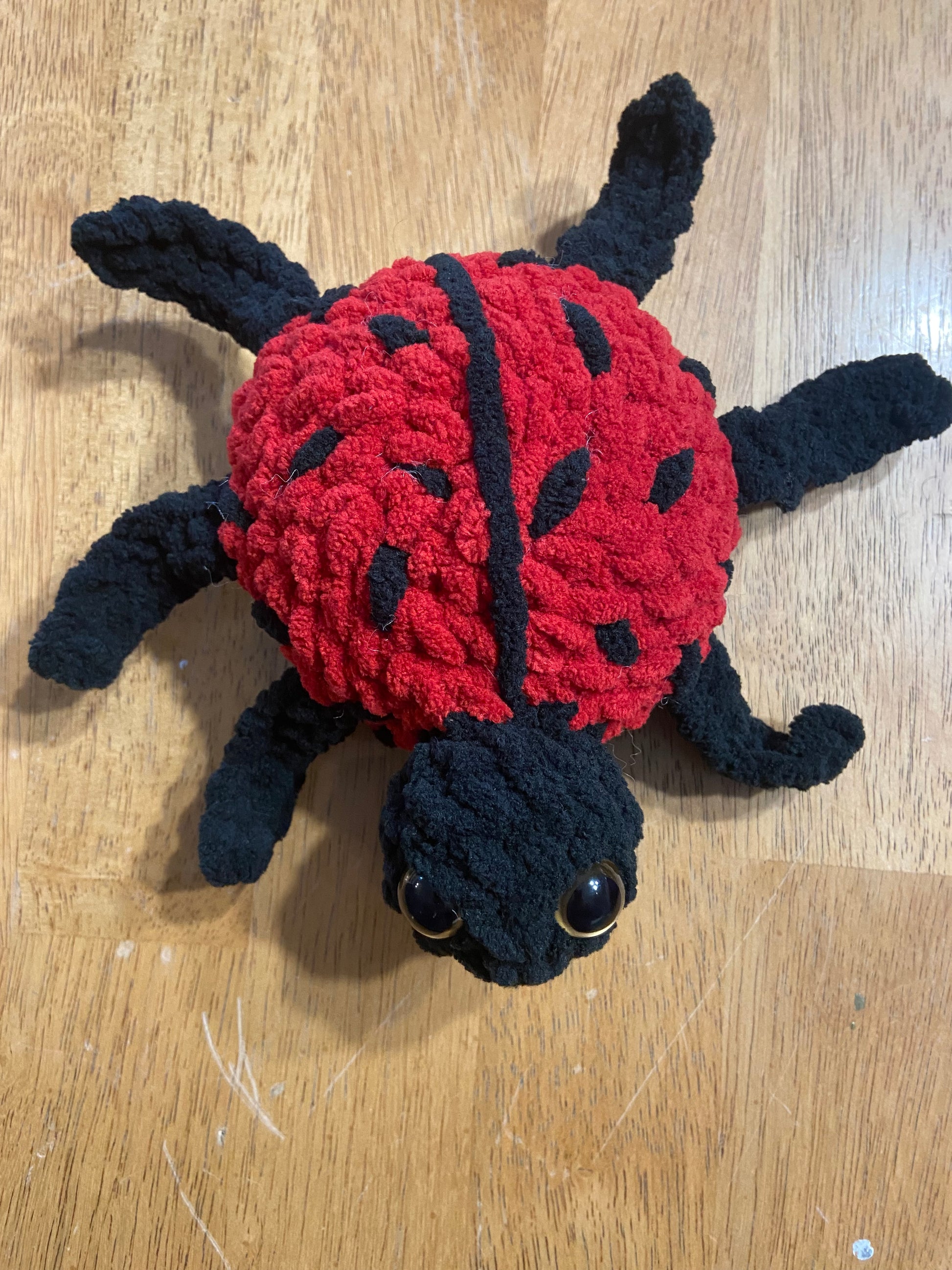 Handmade crochet ladybug plush toy with vibrant red and black colors, adorable design, and huggable texture.
